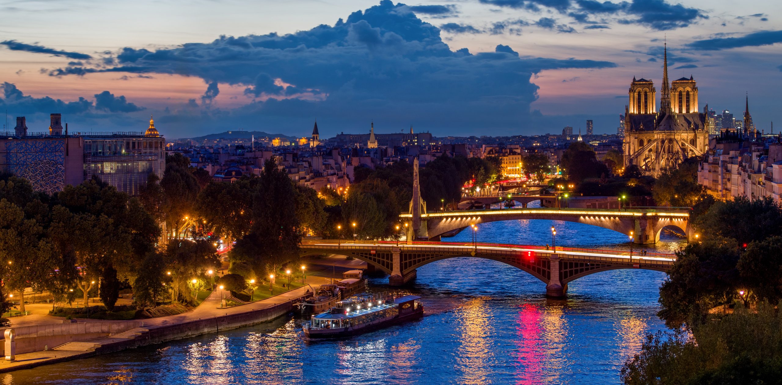 Vue panoramique de Paris au crépuscule, avec la Seine et Notre-Dame illuminées, idéale pour un dîner croisière offrant une expérience magique et romantique | Paris en Scène