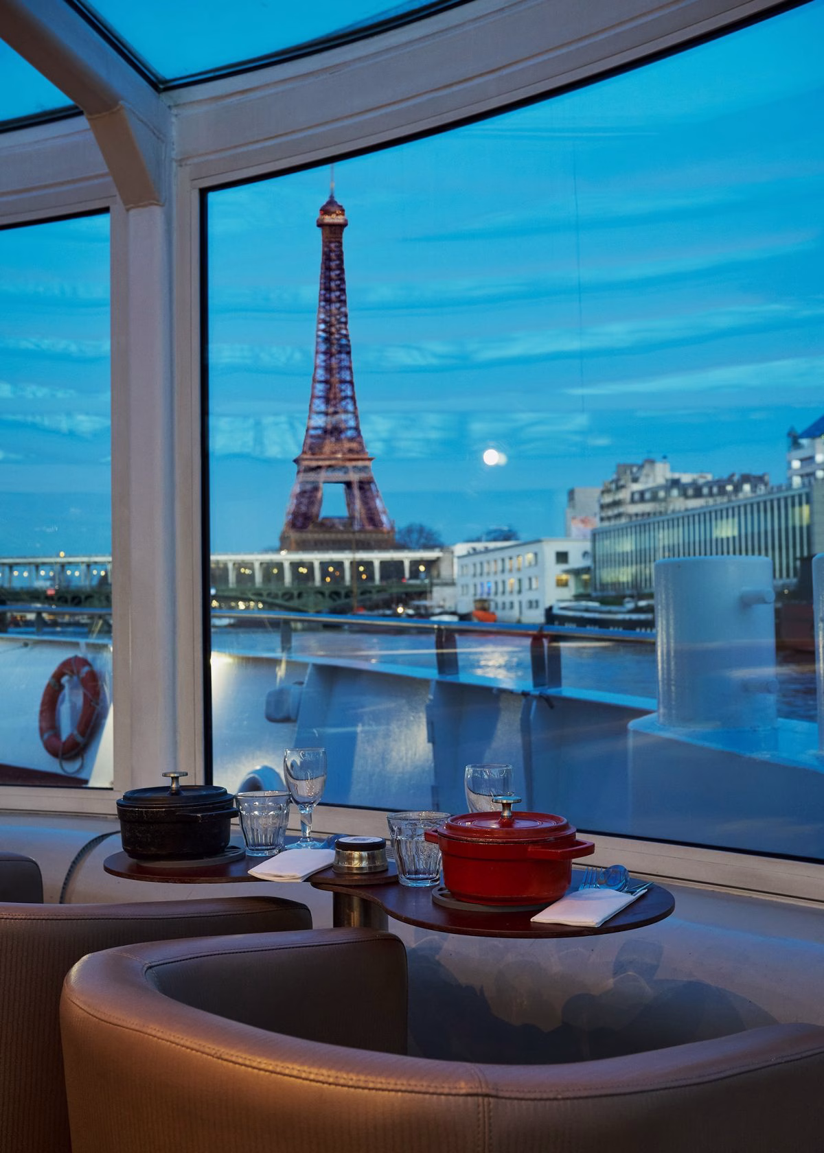 Table dressée avec cocotte émaillée et ambiance feutrée avec vue sur la Tour Eiffel lors d'un diner croisière intime sur la Seine | Paris en Scène
