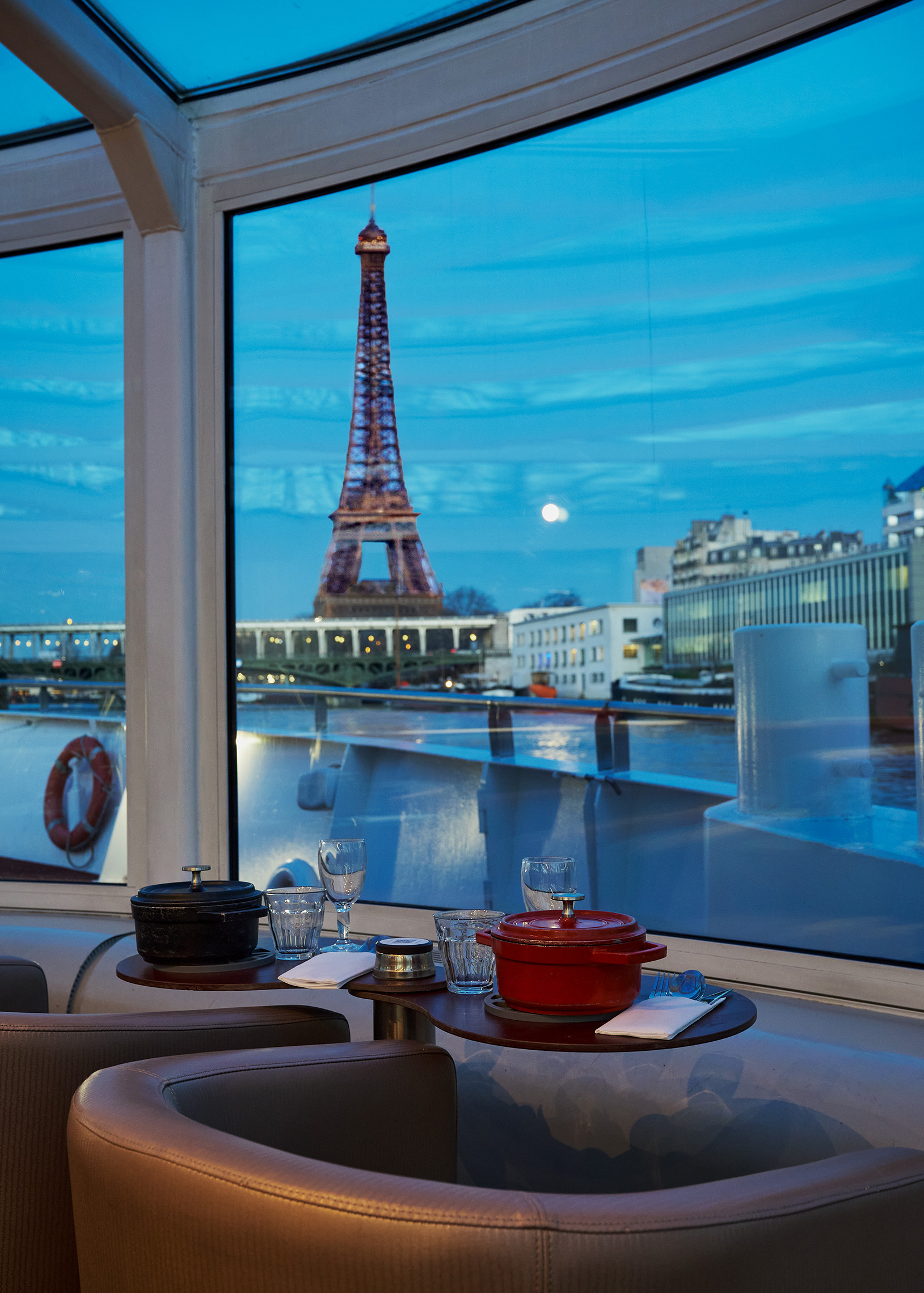 Table dressée avec cocotte émaillée et ambiance feutrée avec vue sur la Tour Eiffel lors d'un diner croisière intime sur la Seine | Paris en Scène